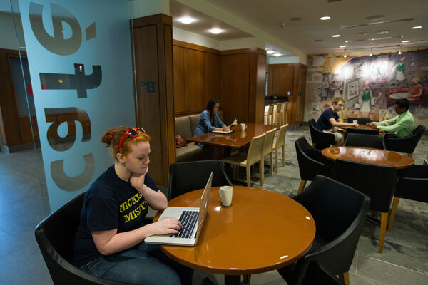 A student using a laptop at a table in front of a glass sign that says "cafe"