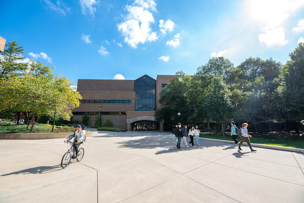 The EECS building on a sunny day with people walking and biking in front of it