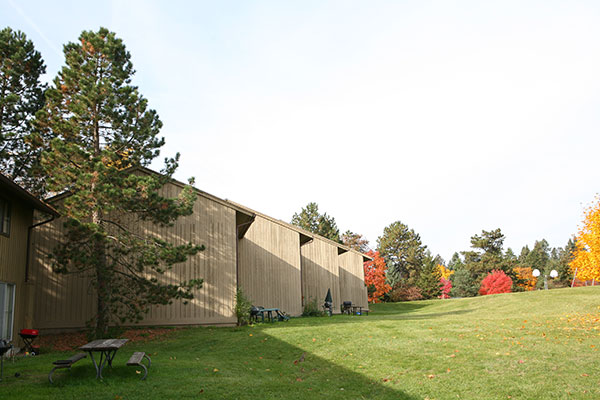 The angled rooflines of several wooden apartment buildings in a row with autumn foliage behind them